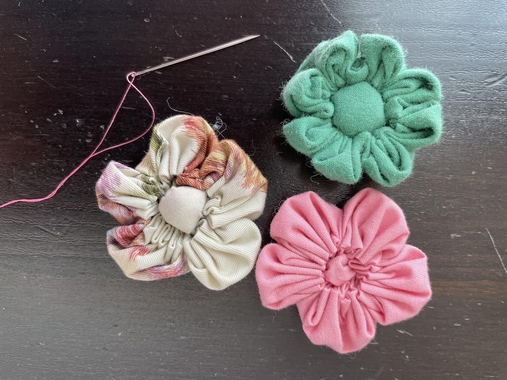 Needle and thread next to handmade flowers in green, pink, and multi-colors, project Luna would use to teach sewing