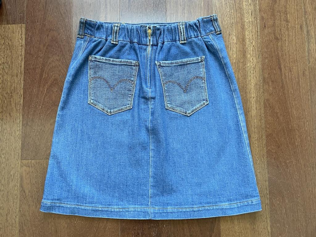 Diy denim skirt back view showing zipper, elastic waist, and pockets, on the wooden floor