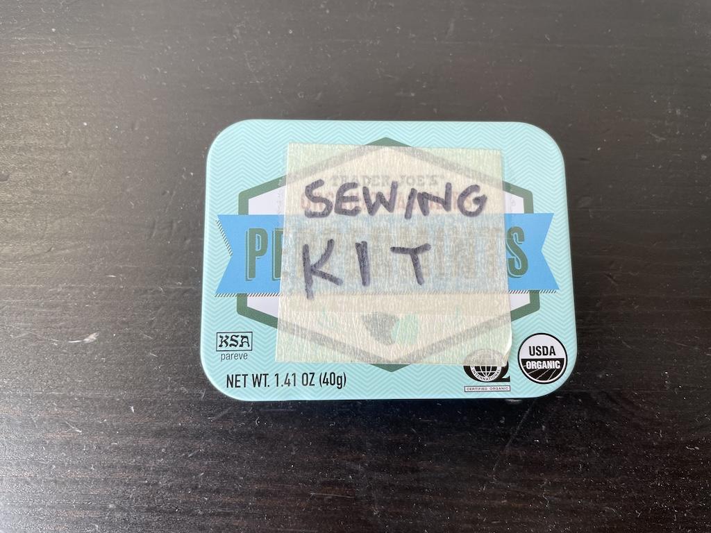 Luna's mint tin with tape over it that says, “sewing kit” on black table