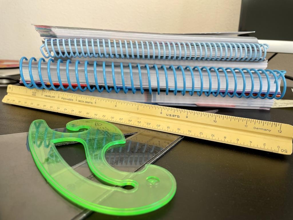 Drafting materials that can be used in making sewing patterns such as ruler, curve, and triangle on a desk with books
