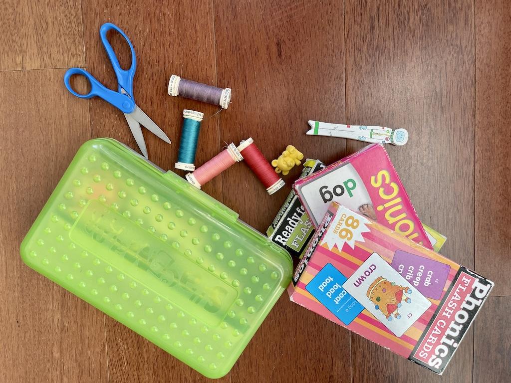 School supplies with pencil box, scissors, phonics flash cards, eraser, and thread on a wooden floor