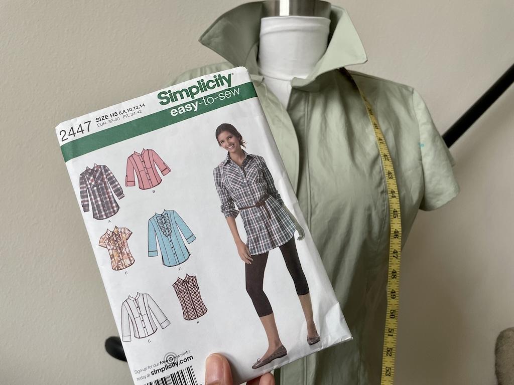 Luna holding up Simplicity S2447 sewing pattern to her unfinished button up shirt on the dress form