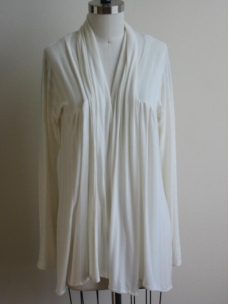 Front view of Luna’s cardigan made from white knit fabric hanging on the dress form