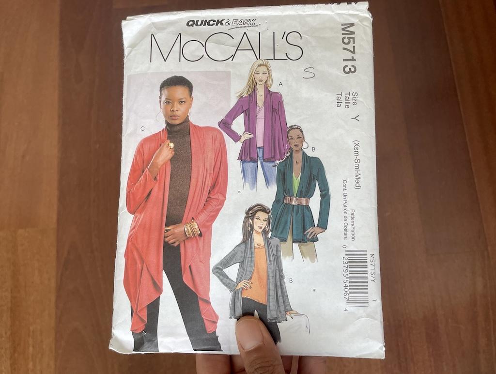 Luna’s hand holding McCall’s M5713 sewing pattern envelope with models wearing finished cardigan pictured.