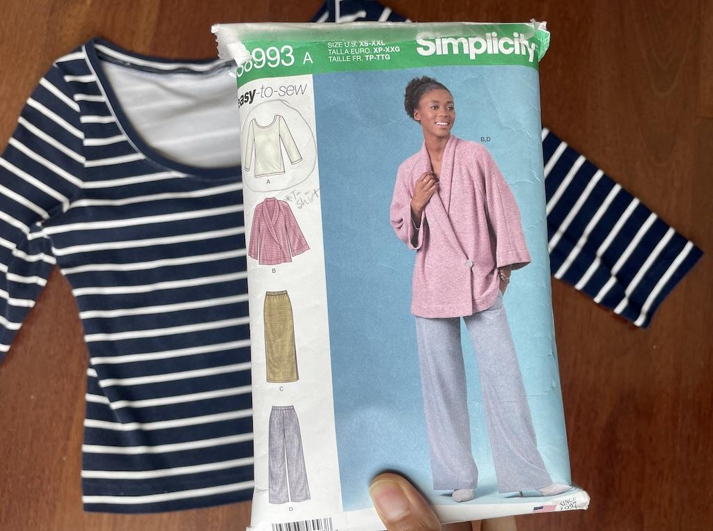 Luna’s hand holding Simplicity S8993 sewing pattern envelope with her striped knit top in the background