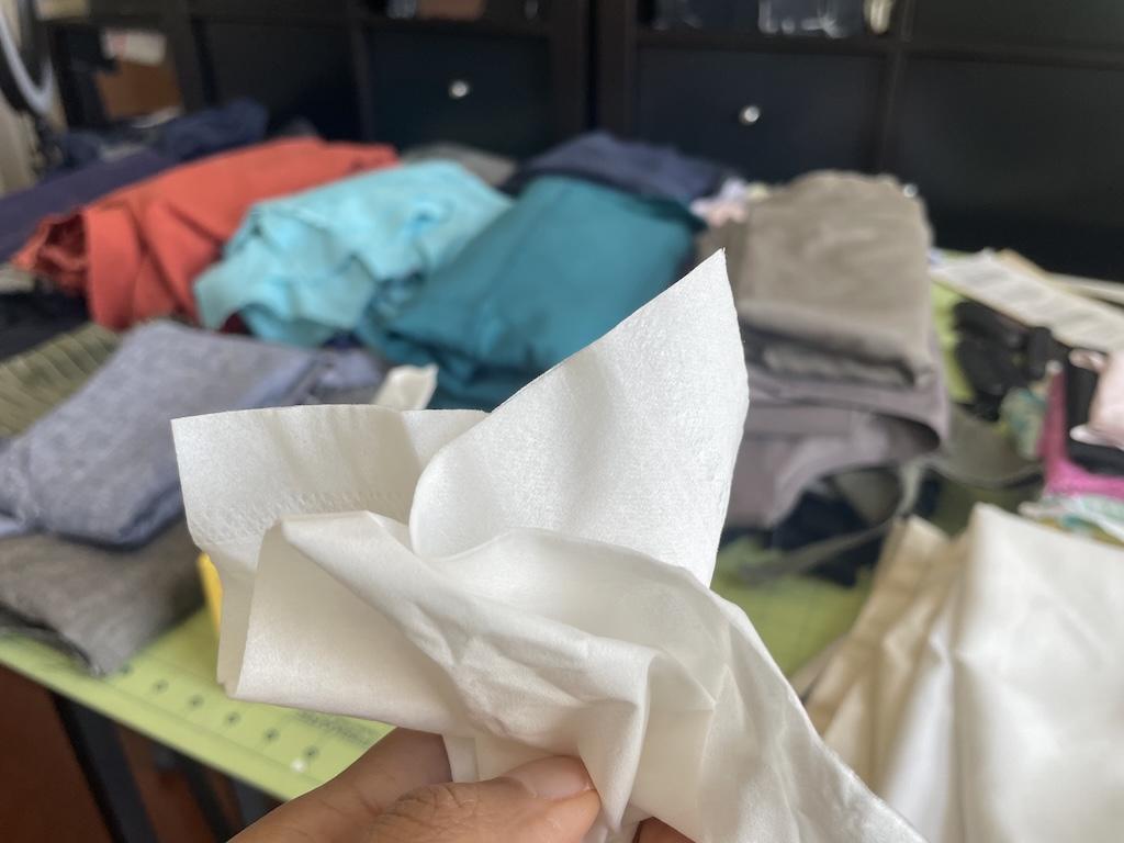 Close up of tissue in Luna’s hand with stacks of fabric in the background