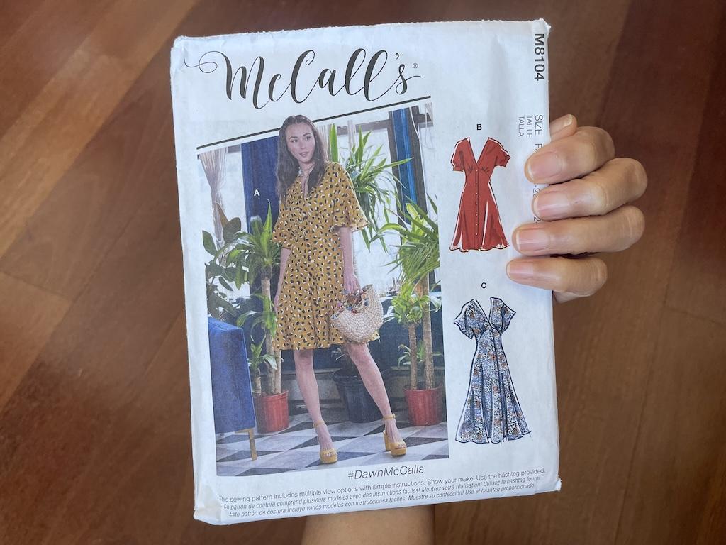 Luna’s hand holding McCall’s M8104 sewing pattern envelope showing model wearing finished dress