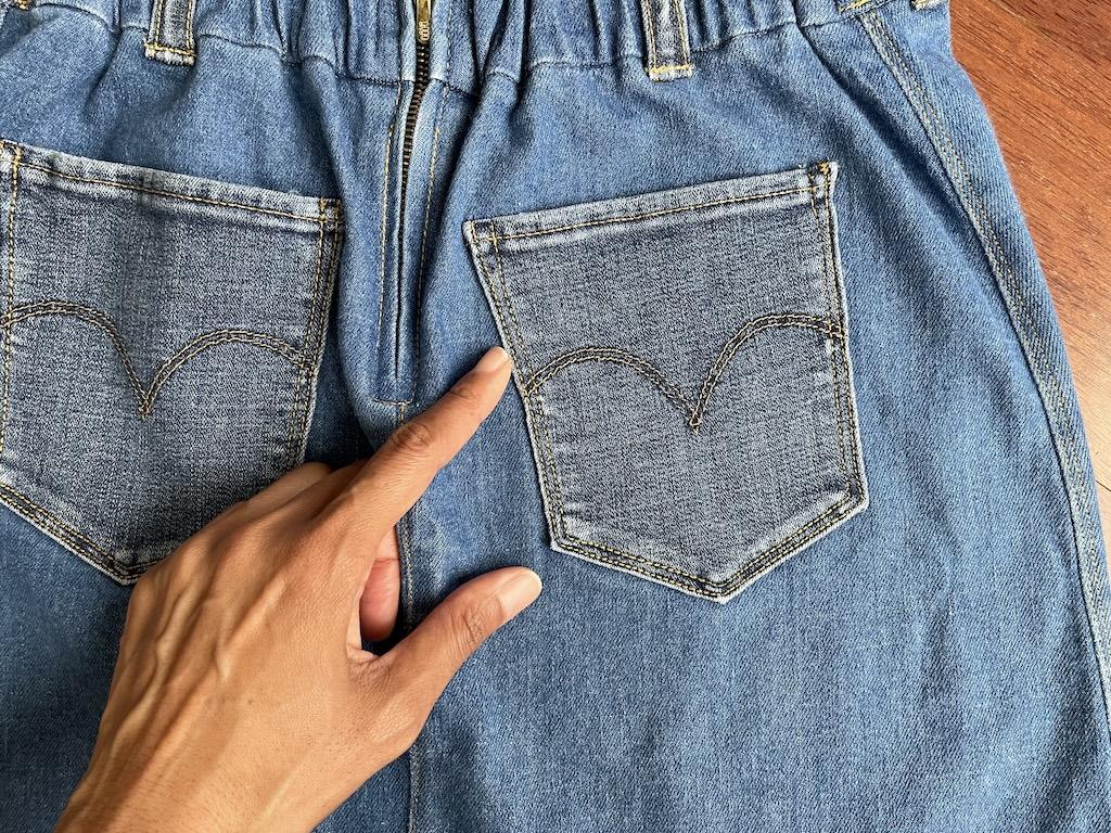 Close up of the back patch pockets on Luna’s denim skirt with her finger pointing to the topstitching
