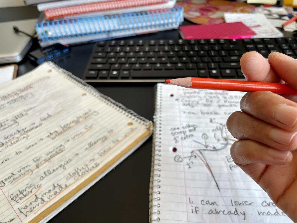 Notebooks with notes written in them and close up of Luna’s hand with keyboard and books in the background
