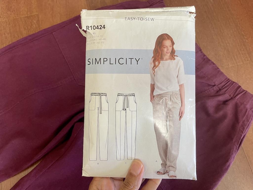 Luna’s hand holding Simplicity S9050 sewing pattern envelope with her pants in the background