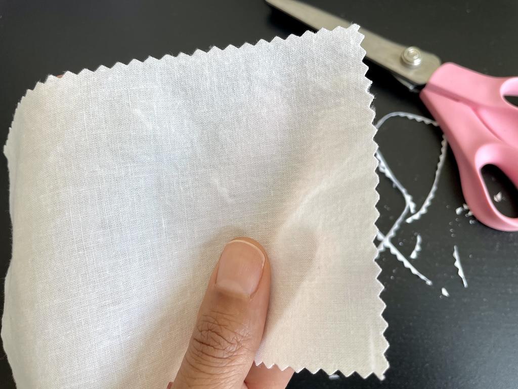 Close up view of Luna’s hand holding fabric swatch with finished edges with zag-zag