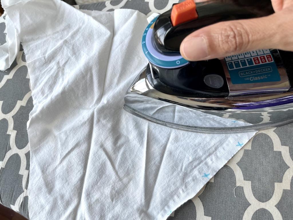 Close up of Luna’s hand ironing muslin fabric to get the wrinkles out