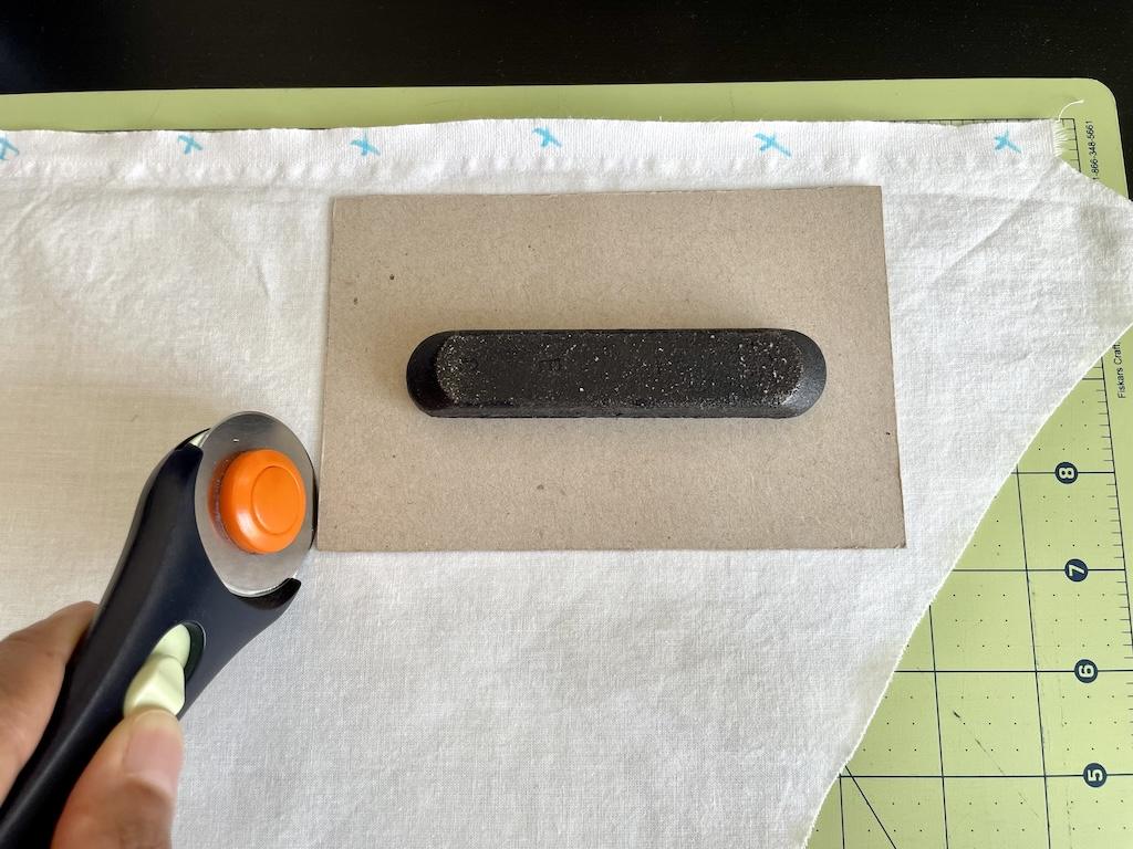 Close up of Luna’s hand holding a rotary cutter, showing fabric, template, and pattern weight on cutting mat