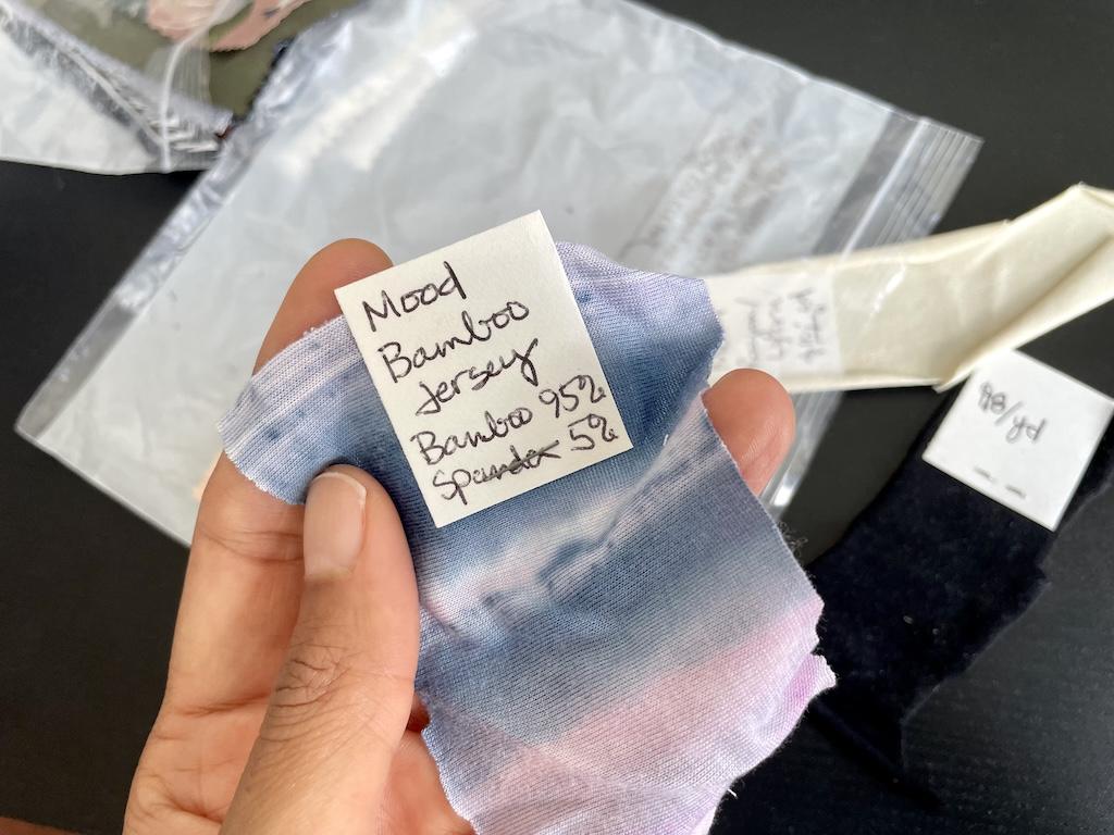 Close up of Luna’s hand holding her fabric swatch with tag stapled on it