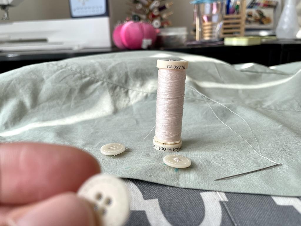 View of Luna’s hand holding button, with needle and thread in background on her shirt