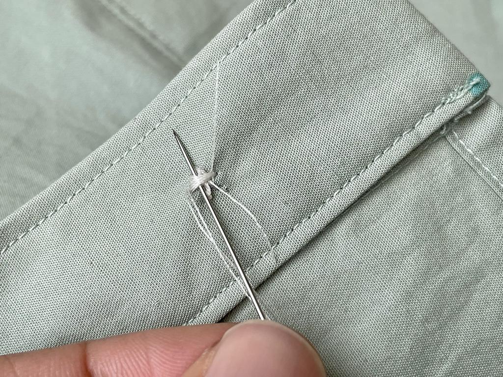 Close up view of Luna’s fingers taking needle through back side of fabric loops of sewn button