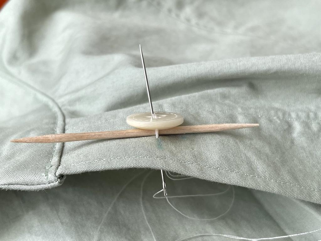 Close up side view of Luna’s fingers pushing needle through button with the toothpick underneath