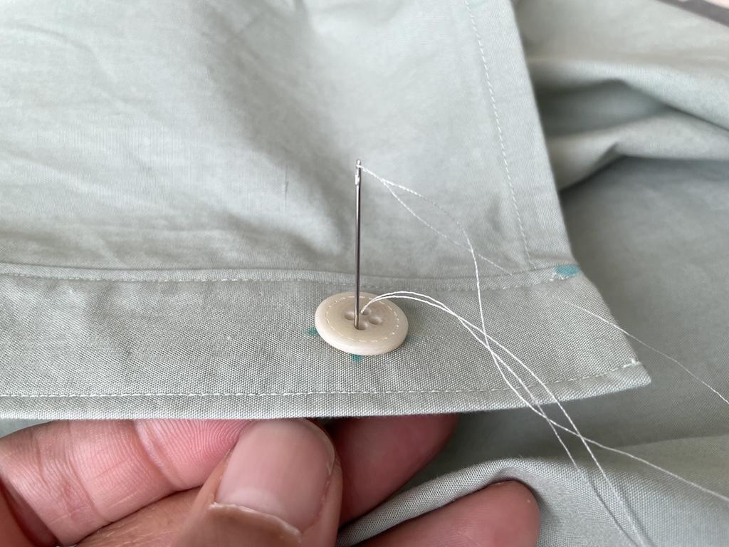 Close up view of Luna’s fingers and needle and thread going through opposite hole on button