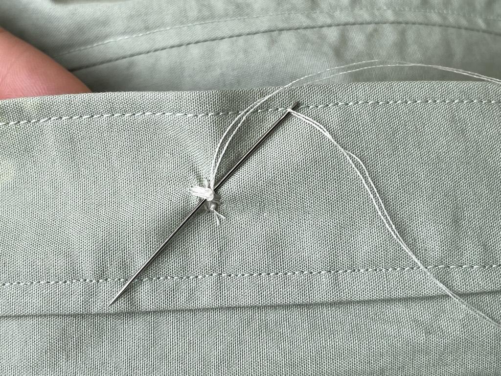 Close up of pulling needle through back side of sewn button loops to secure thread