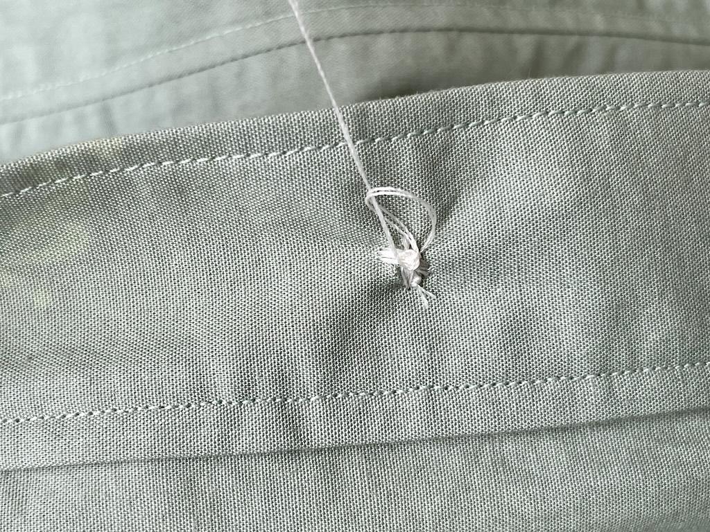 Close up of pulling thread through loop to make a knot on back side of sewn button to secure thread