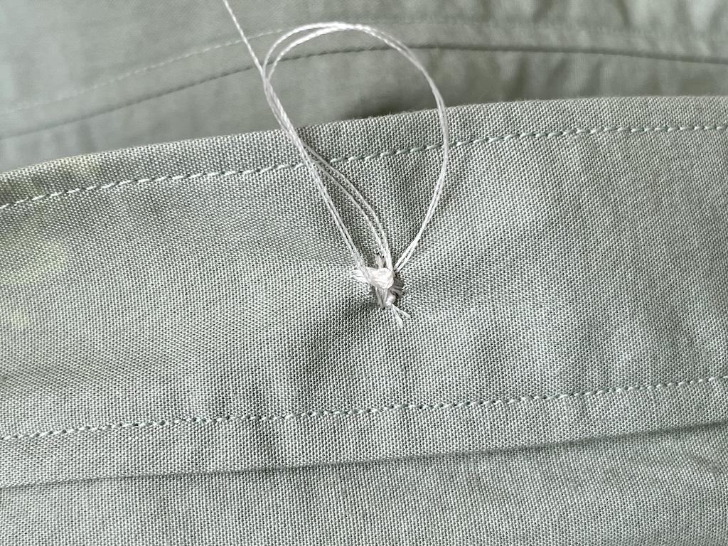 Close up of pulling thread through loop to make a knot on back side of sewn button to secure thread
