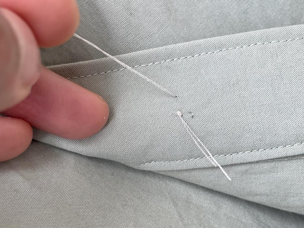 Close up view of Luna’s fingers and thread being pulled out back side of fabric with knot