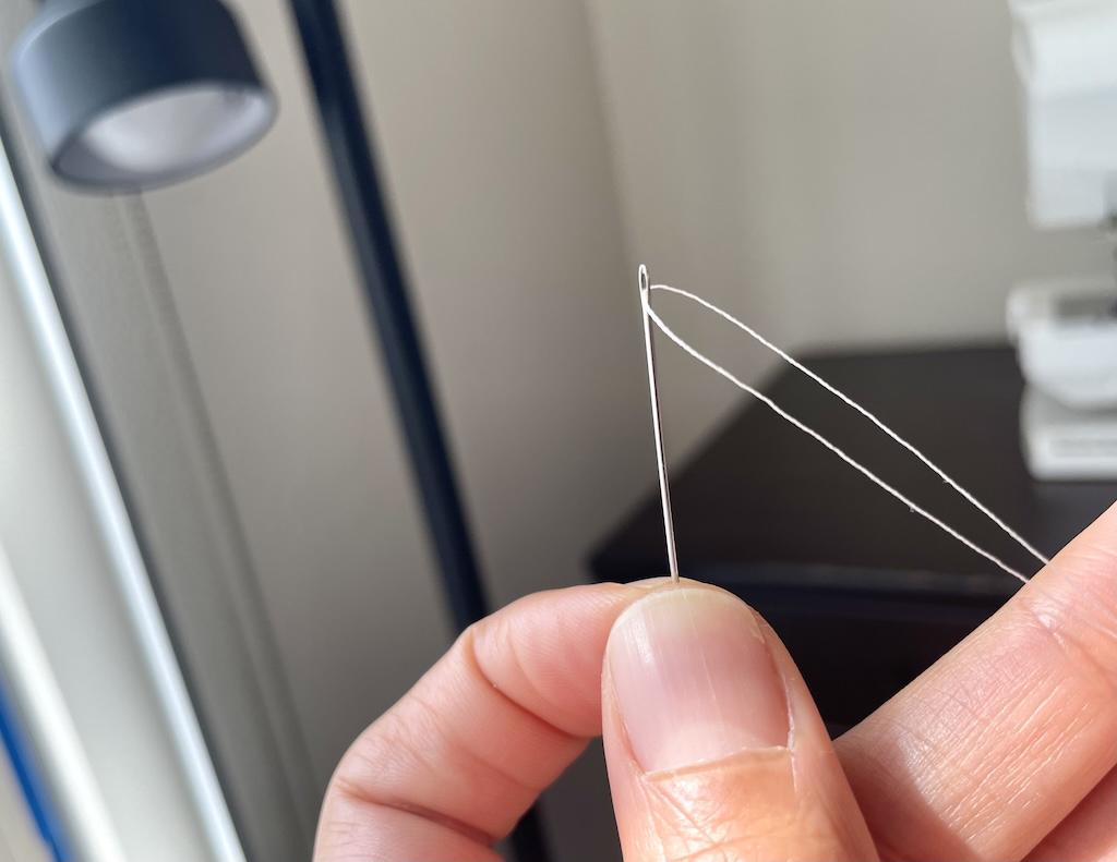 Close up view of Luna’s hand holding thread in eye of needle and doubled