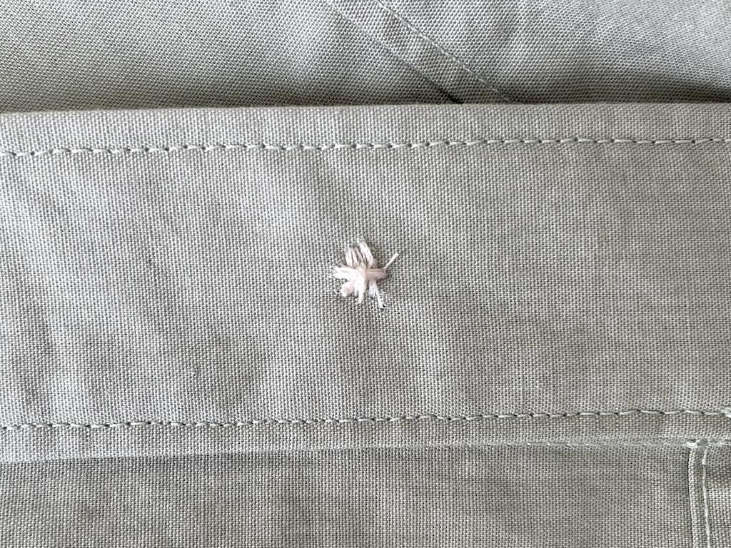 Close up of knot made on stitches on back side of fabric of button Luna hand sewed, with long strands cut