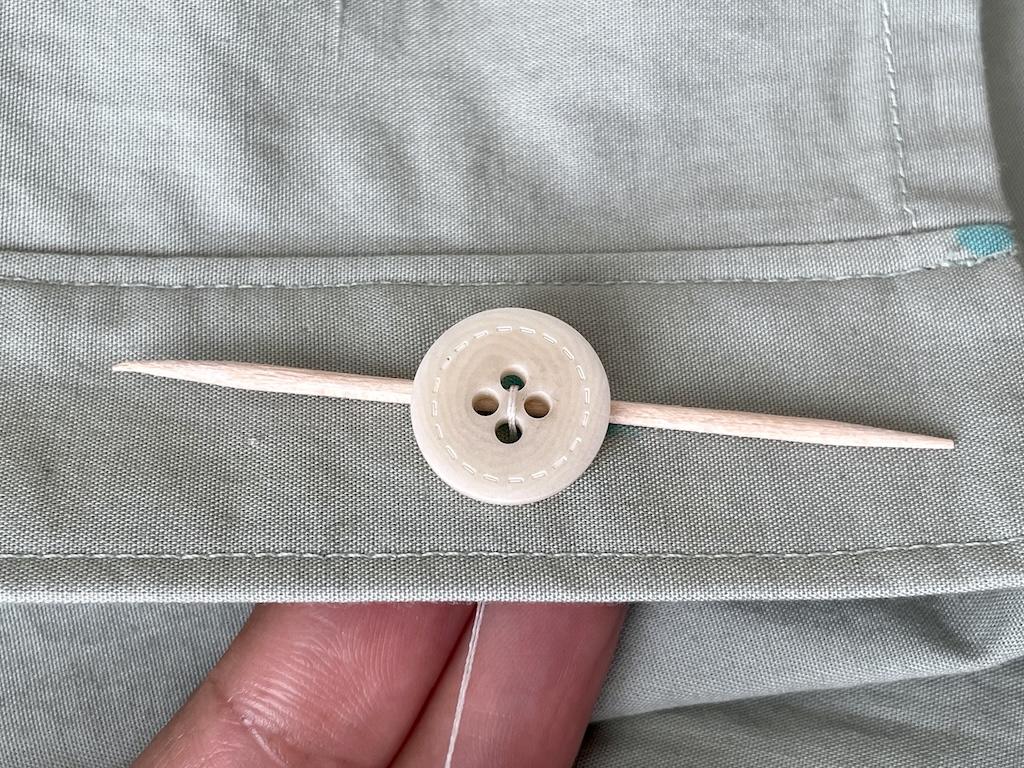 Close up view of Luna’s fingers and button with toothpick under it on her shirt