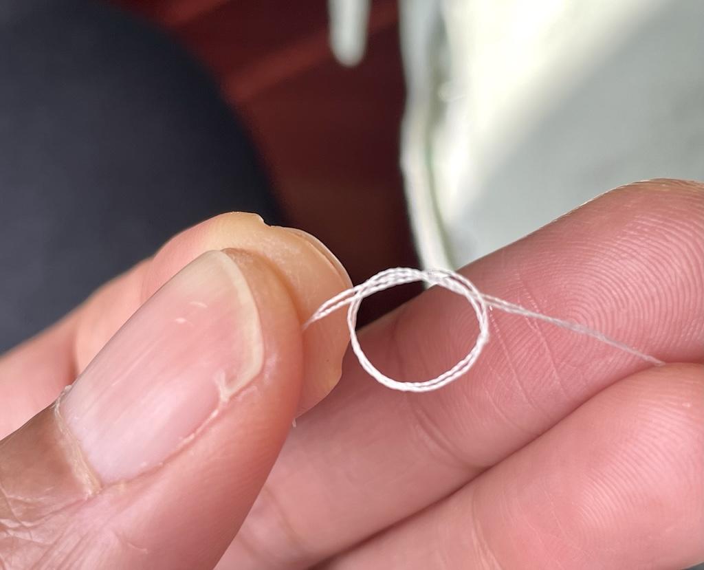 Close up view of Luna’s fingers tying knot at the end of thread ends