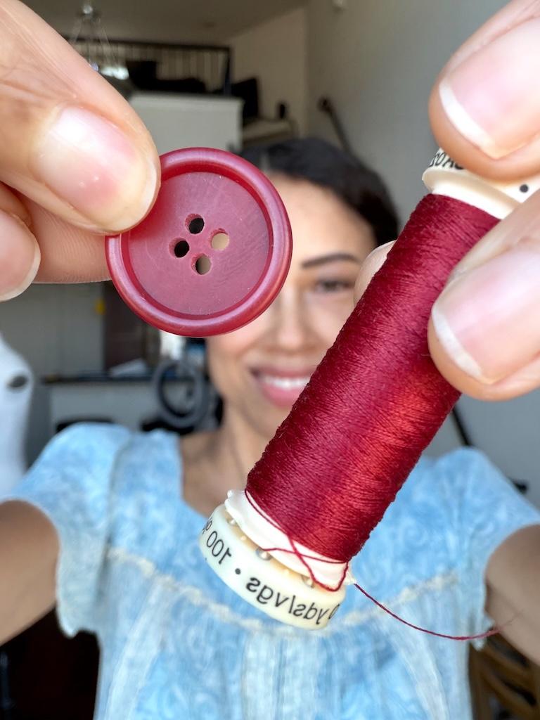 Luna smiling and holding up 4-hole button and matching thread to camera