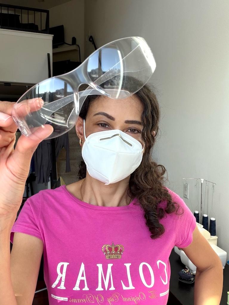 Luna holding up safety glasses and wearing a mask when sewing