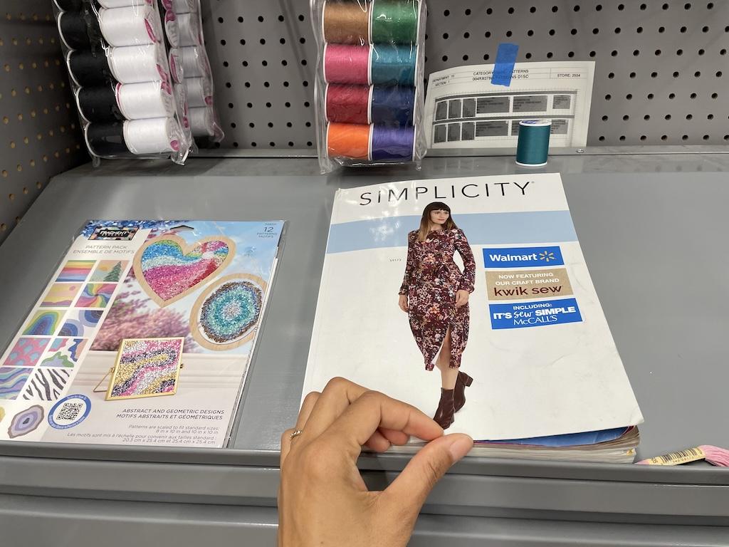 Luna’s hand flipping through the Simplicity sewing pattern catalogue at Walmart