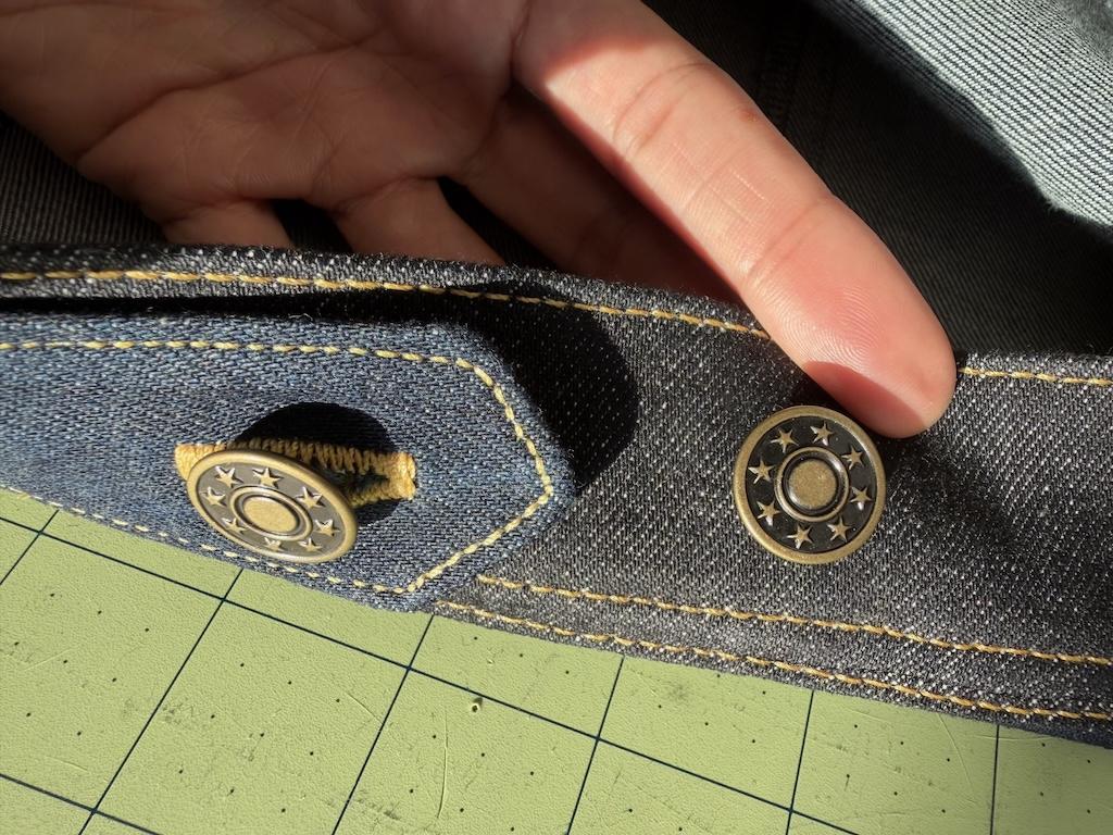 Close up view showing fingers and attached jeans button cap to jacket that Luna made