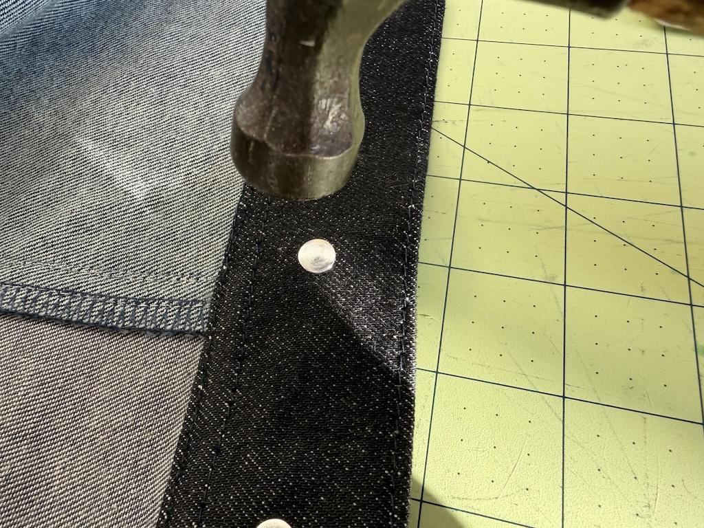 Close up view of hammer head about to hit jeans button tack to attach it to jacket