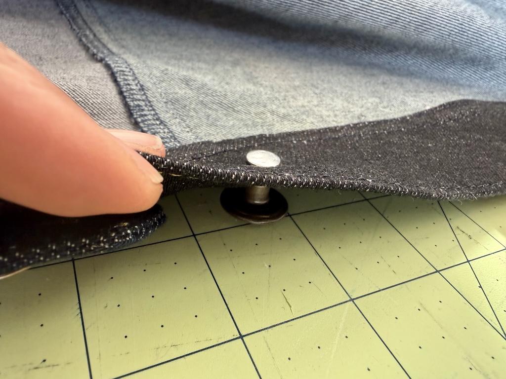 View of Luna’s fingers turning jeans button so that the top of cap is face down on cutting mat