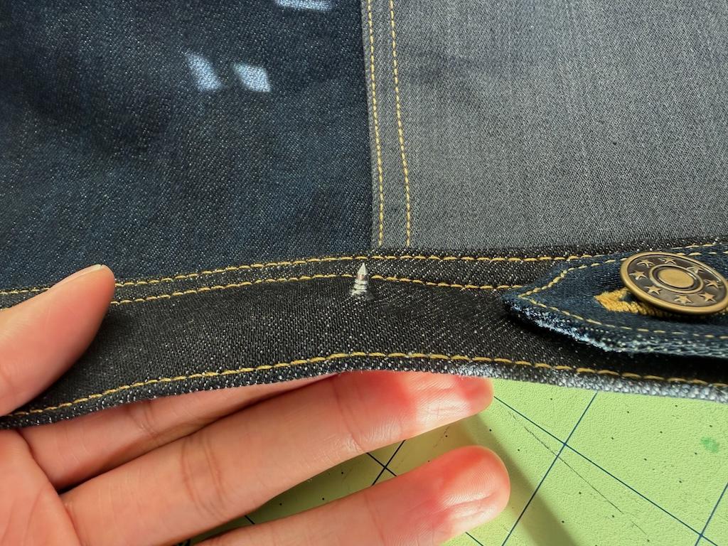 Close up of tack of jeans button that Luna pushed through fabric of jacket