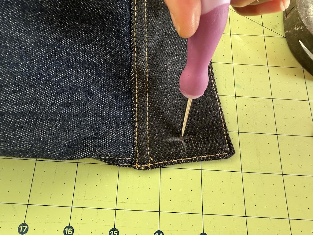 Close up of awl and Luna making hole on jacket to attach the jeans button