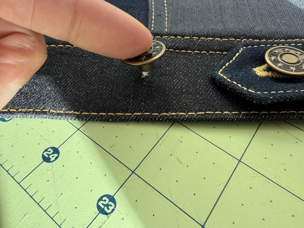 Close up of Luna’s finger putting the cap on the tack of the jeans button on the jacket she made