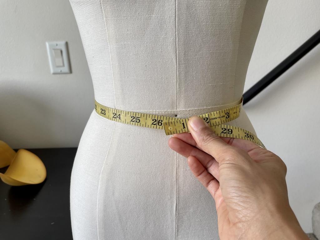Luna’s hand measuring the waist of the dress form with measuring tape